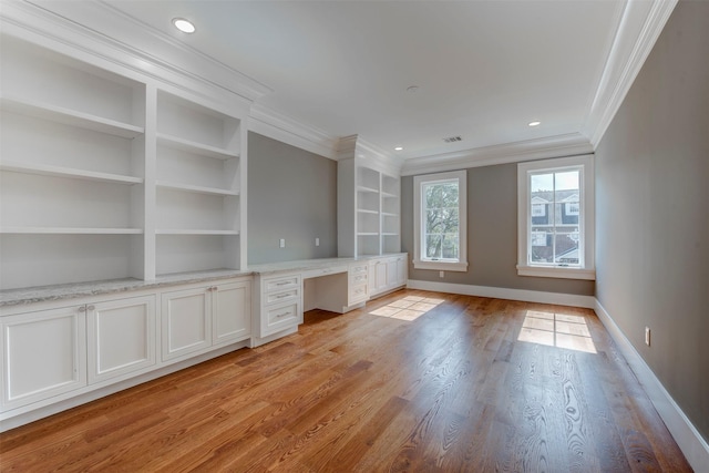 unfurnished office featuring built in shelves, ornamental molding, built in desk, and light hardwood / wood-style flooring