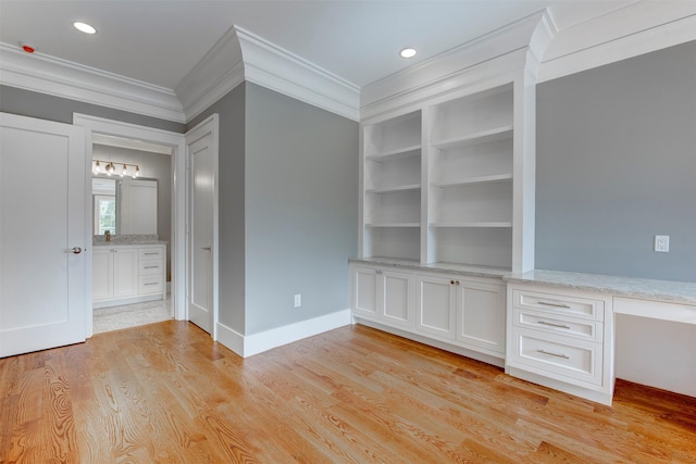 interior space with built in features, built in desk, ornamental molding, and light wood-type flooring