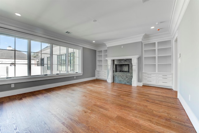 unfurnished living room featuring built in features, a high end fireplace, ornamental molding, and light wood-type flooring