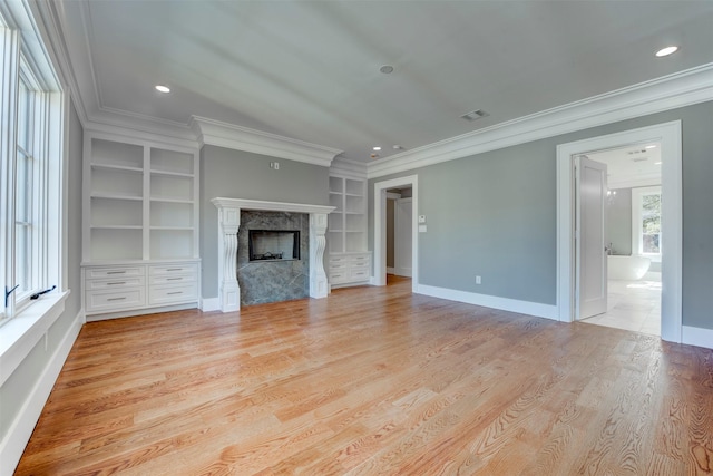 unfurnished living room with crown molding, built in features, a fireplace, and light hardwood / wood-style flooring