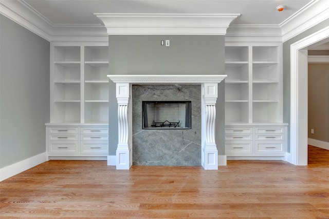 unfurnished living room featuring crown molding, built in features, a high end fireplace, and light hardwood / wood-style flooring