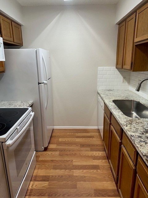 kitchen with backsplash, sink, light stone counters, light wood-type flooring, and white appliances