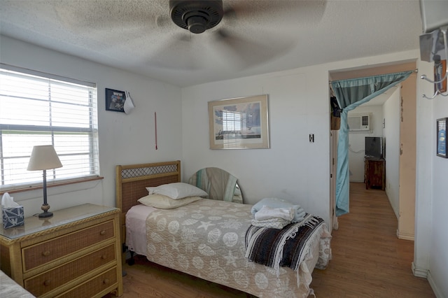 bedroom featuring a textured ceiling, wood-type flooring, ceiling fan, and a wall unit AC