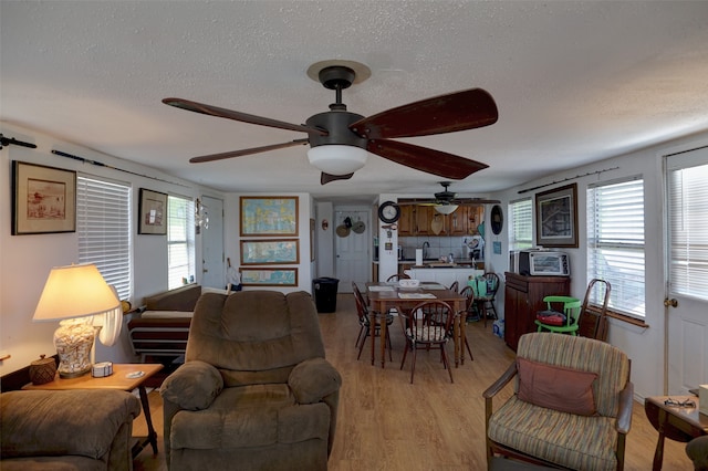 living room with ceiling fan, a textured ceiling, light hardwood / wood-style floors, and a healthy amount of sunlight