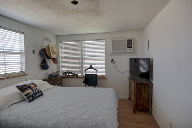 bedroom with a textured ceiling, light hardwood / wood-style flooring, and an AC wall unit