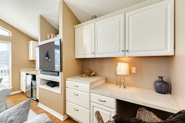 kitchen with light wood-type flooring, built in desk, lofted ceiling, white cabinetry, and stainless steel dishwasher