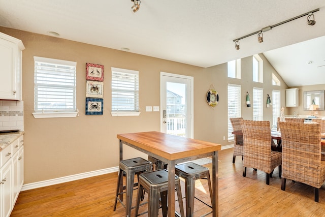 dining space with light wood-type flooring, rail lighting, vaulted ceiling, and plenty of natural light