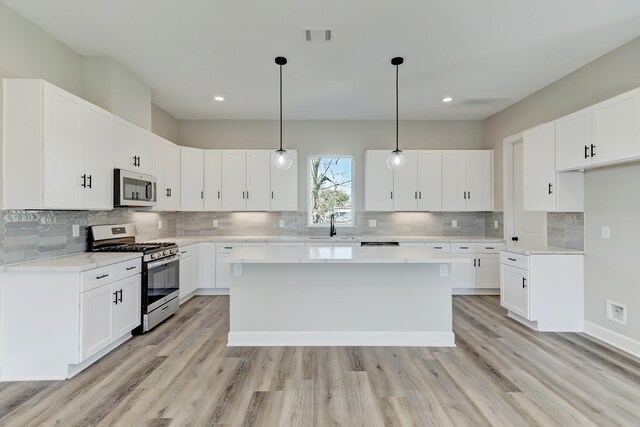 kitchen with white cabinets, appliances with stainless steel finishes, light hardwood / wood-style flooring, and hanging light fixtures