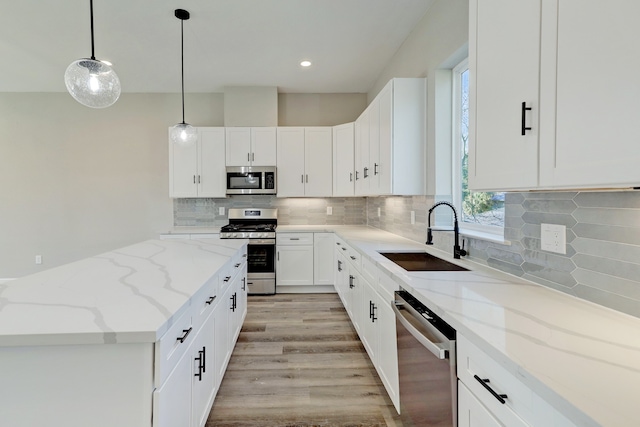 kitchen with appliances with stainless steel finishes, light stone counters, sink, pendant lighting, and white cabinetry