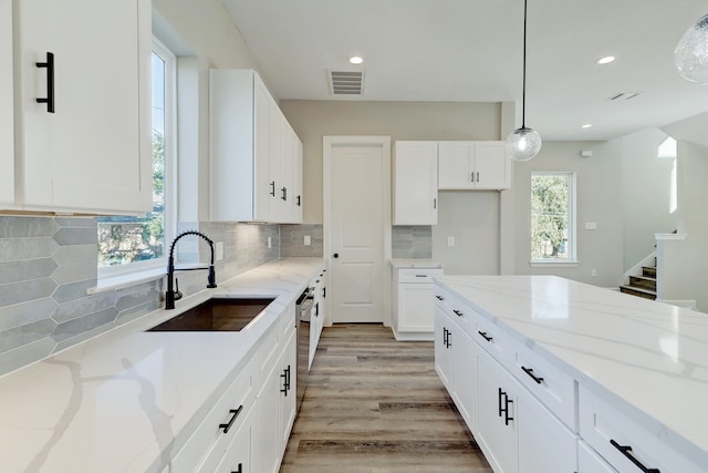 kitchen featuring light stone countertops, sink, pendant lighting, white cabinets, and light hardwood / wood-style floors