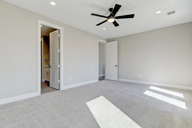 unfurnished bedroom with ceiling fan, ensuite bathroom, and light carpet