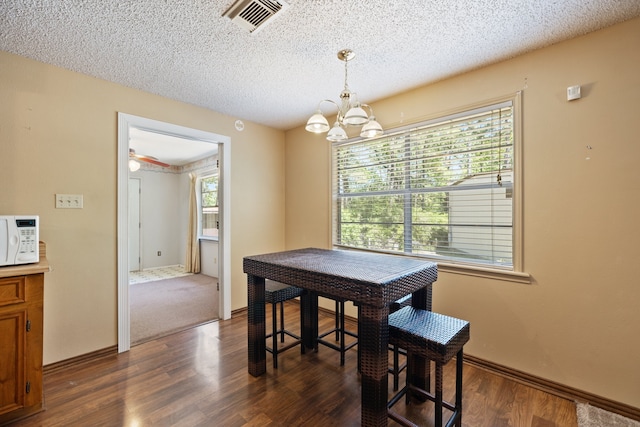 dining space with dark wood-type flooring, a textured ceiling, and an inviting chandelier