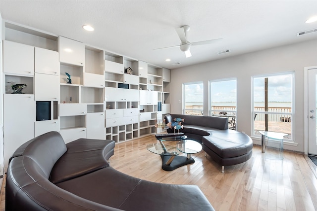 living room featuring ceiling fan, light hardwood / wood-style flooring, and a textured ceiling