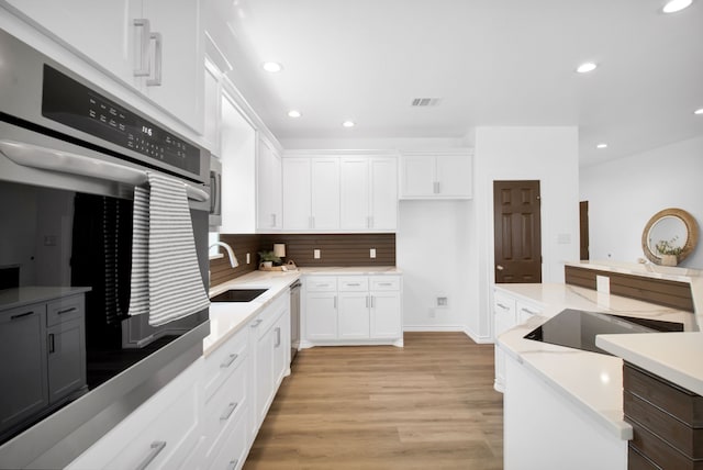 kitchen with light wood-type flooring, backsplash, sink, and white cabinets