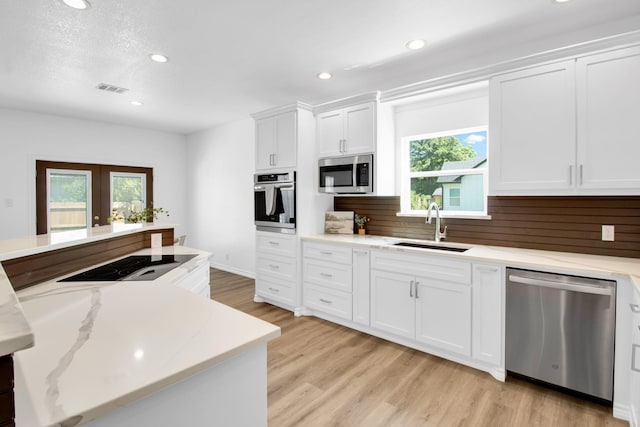 kitchen with appliances with stainless steel finishes, light wood-type flooring, light stone counters, white cabinets, and sink