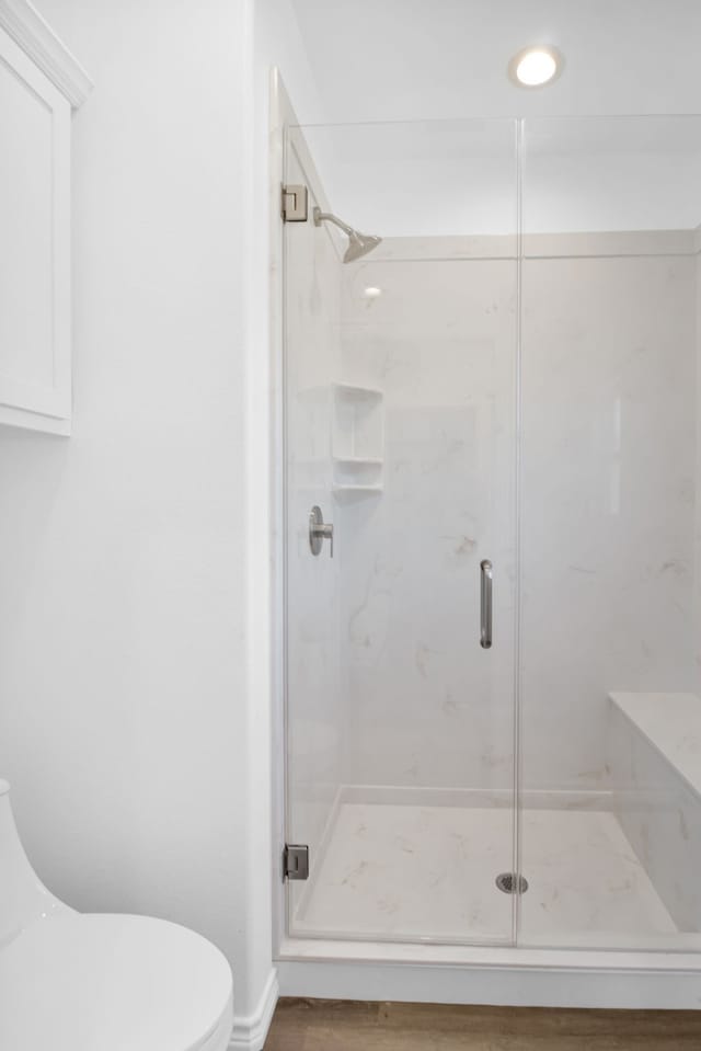 bathroom with a shower with door, hardwood / wood-style floors, and toilet