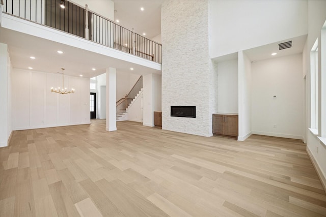 unfurnished living room featuring a stone fireplace, a towering ceiling, light wood-type flooring, and an inviting chandelier