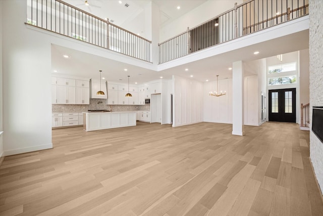 unfurnished living room with ceiling fan, french doors, a towering ceiling, and light hardwood / wood-style floors