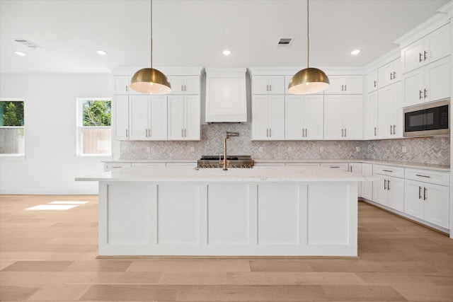 kitchen featuring a kitchen island with sink, premium range hood, stainless steel appliances, and hanging light fixtures