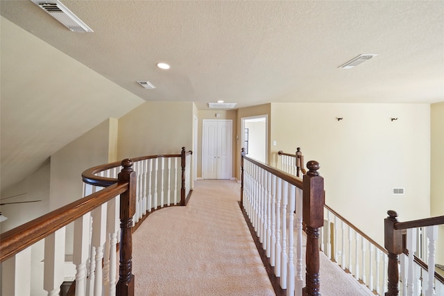 hall featuring light colored carpet, vaulted ceiling, and a textured ceiling