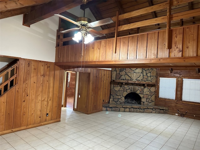 unfurnished living room with a fireplace, ceiling fan, light tile patterned flooring, wood walls, and high vaulted ceiling