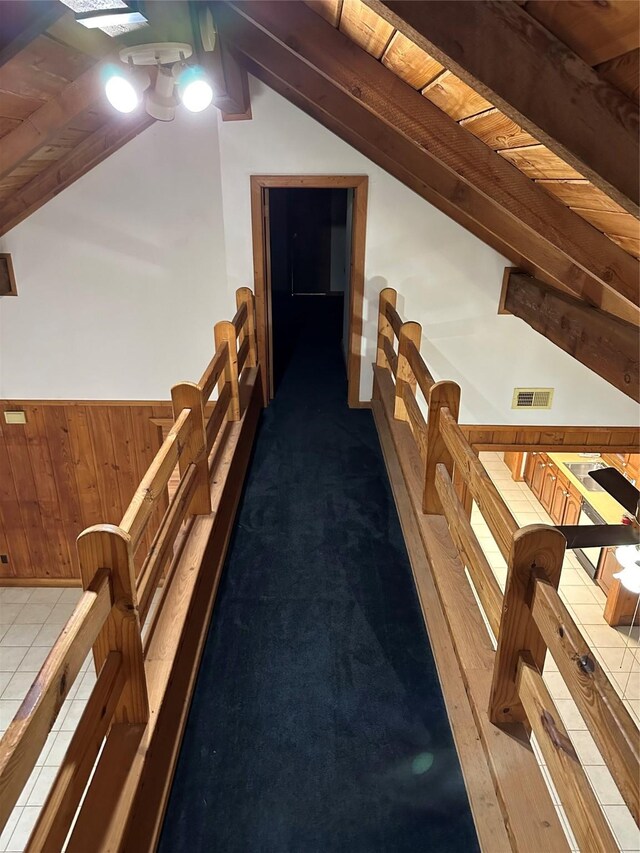 interior space featuring wood walls, dark colored carpet, wooden ceiling, and vaulted ceiling with beams