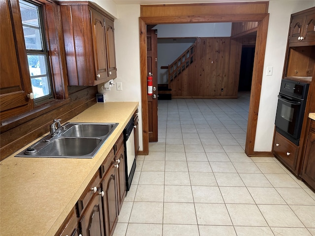 kitchen with black appliances, wood walls, sink, and light tile patterned floors