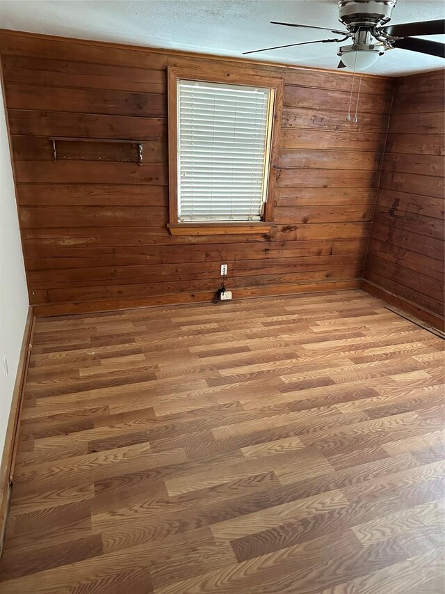 spare room with a textured ceiling, ceiling fan, hardwood / wood-style floors, and wooden walls