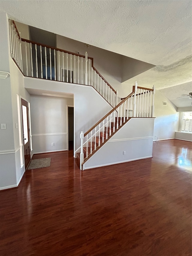 staircase featuring ceiling fan, a high ceiling, a textured ceiling, and dark hardwood / wood-style flooring