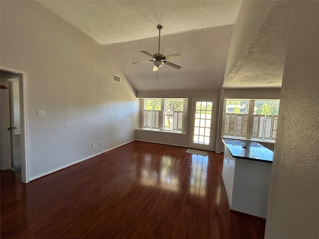 unfurnished living room featuring dark wood-type flooring, a textured ceiling, ceiling fan, and vaulted ceiling