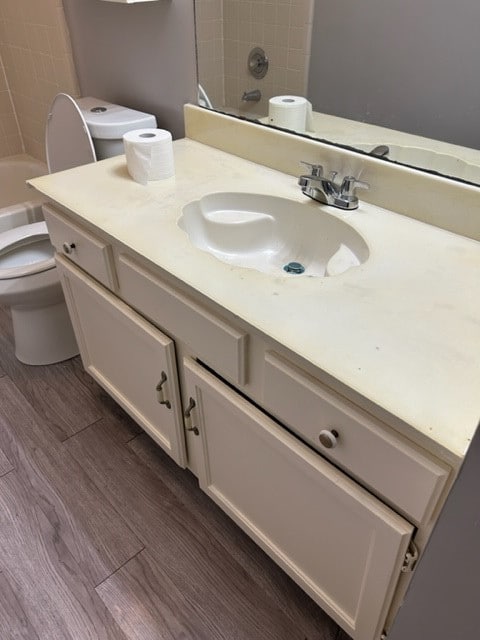 full bathroom with tiled shower / bath, vanity, wood-type flooring, and toilet