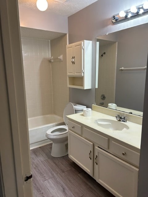 full bathroom with hardwood / wood-style floors, tiled shower / bath, a textured ceiling, toilet, and vanity