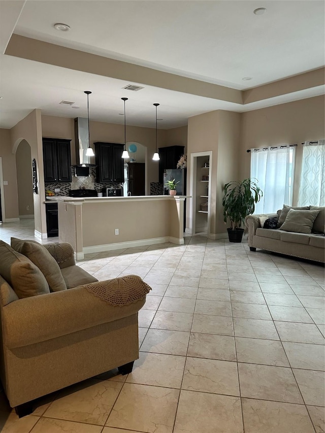 living room featuring arched walkways, baseboards, light tile patterned floors, a tray ceiling, and visible vents