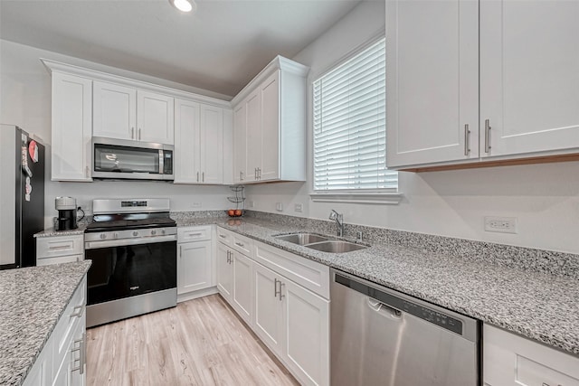 kitchen with sink, white cabinetry, light hardwood / wood-style flooring, stainless steel appliances, and light stone countertops