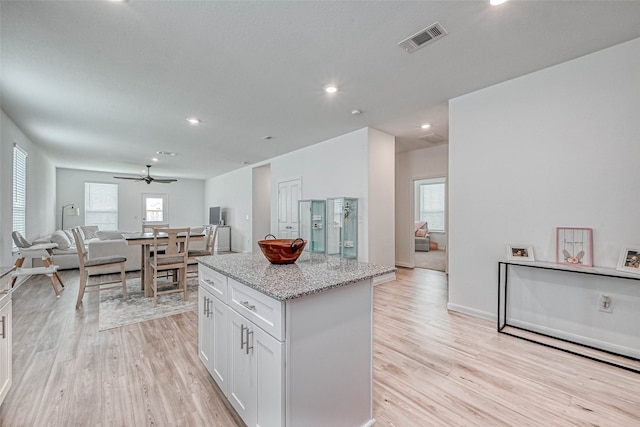 kitchen featuring white cabinetry, light stone countertops, a center island, ceiling fan, and light hardwood / wood-style flooring