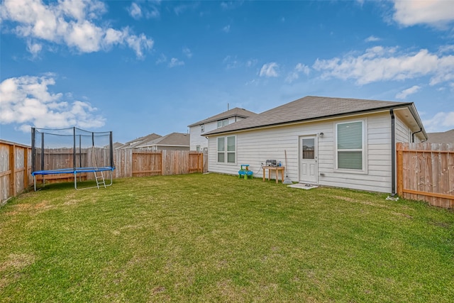 back of property with a trampoline and a yard