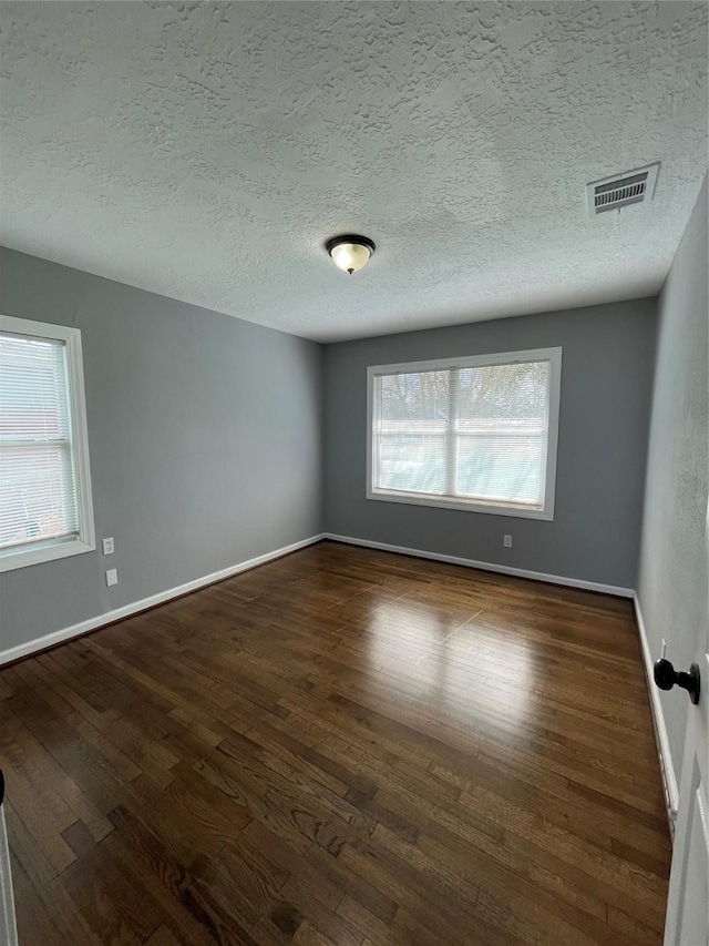 spare room with a textured ceiling, dark hardwood / wood-style flooring, and a healthy amount of sunlight