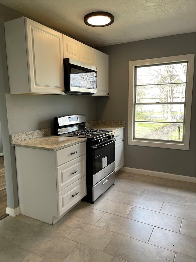 kitchen with appliances with stainless steel finishes, light stone counters, a textured ceiling, white cabinets, and light tile patterned flooring