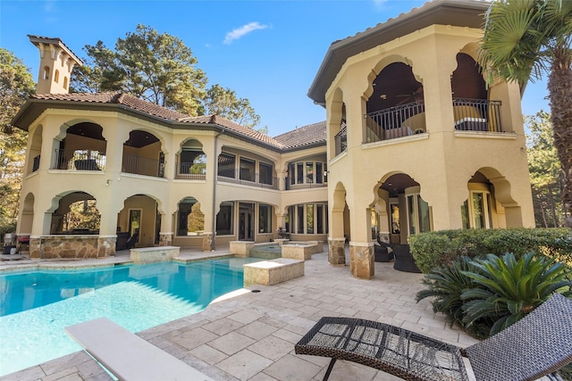 rear view of house featuring a patio area, a balcony, and a pool with hot tub