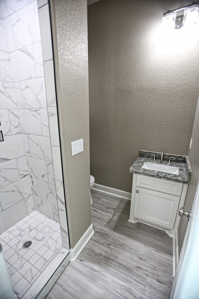 bathroom featuring wood-type flooring, vanity, toilet, and tiled shower