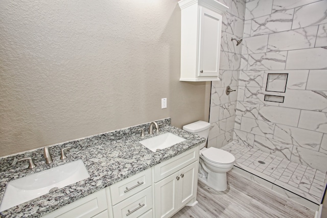 bathroom with vanity, toilet, hardwood / wood-style flooring, and tiled shower