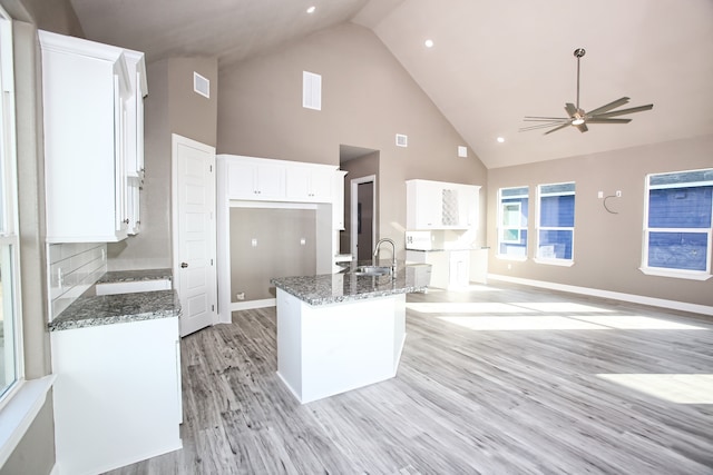 kitchen featuring ceiling fan, white cabinets, high vaulted ceiling, dark stone countertops, and light wood-type flooring