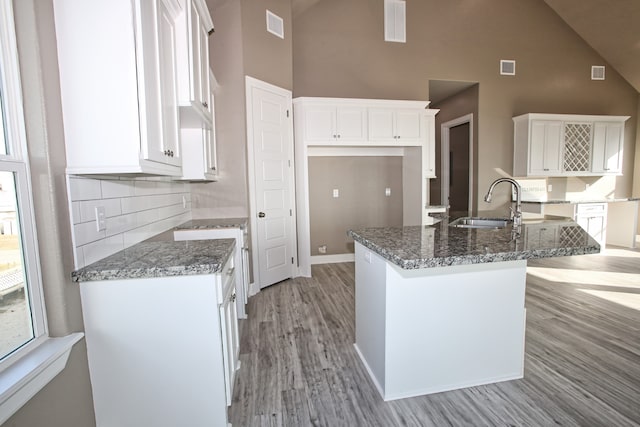 kitchen with dark stone counters, light hardwood / wood-style floors, sink, white cabinetry, and high vaulted ceiling