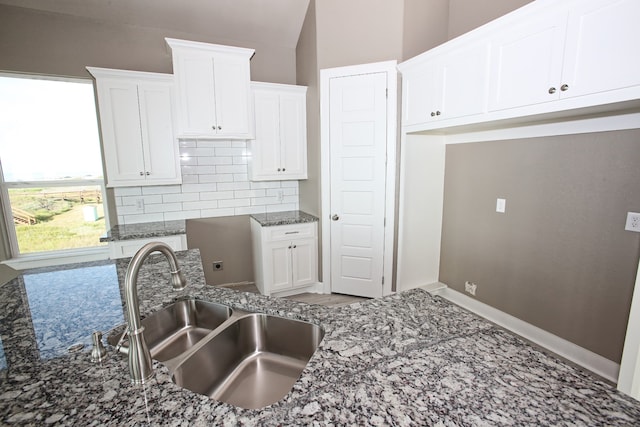 kitchen featuring decorative backsplash, dark stone countertops, white cabinetry, vaulted ceiling, and sink