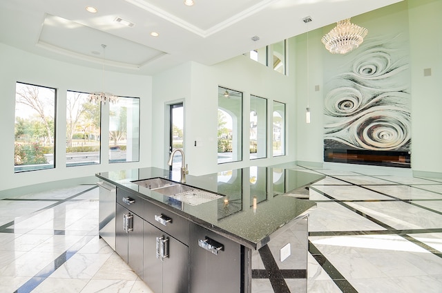 kitchen featuring light tile floors, an inviting chandelier, a center island with sink, a tray ceiling, and sink