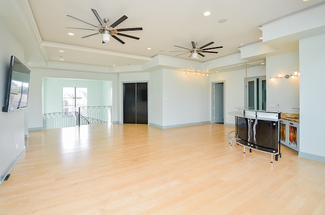 living room featuring elevator, ceiling fan, light hardwood / wood-style floors, a raised ceiling, and crown molding