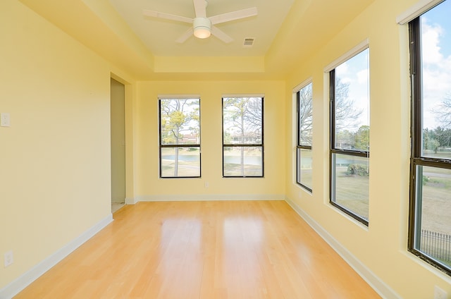 unfurnished room featuring light hardwood / wood-style floors, ceiling fan, a tray ceiling, and a wealth of natural light