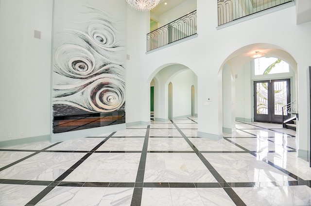 tiled entrance foyer featuring french doors, a notable chandelier, and a towering ceiling