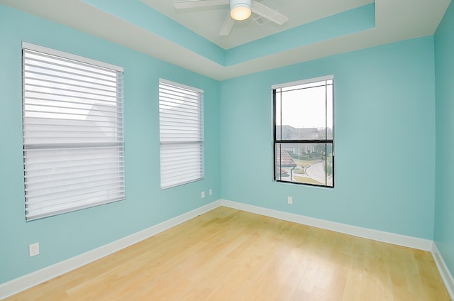 spare room with plenty of natural light, a tray ceiling, ceiling fan, and light hardwood / wood-style flooring