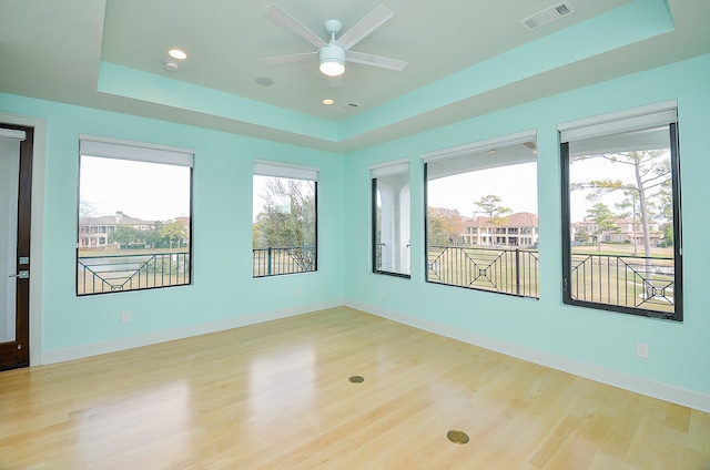 spare room with a raised ceiling, ceiling fan, and light wood-type flooring